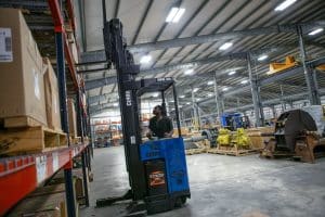 Worker operating a forklift inside a warehouse filled with industrial equipment and boxed materials, representing Tulco’s short-term industrial storage solutions.