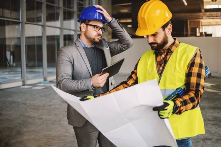 operational continuity - Supervisor getting upset about works. Construction site worker holding blue prints and looking at it. Something got wrong.